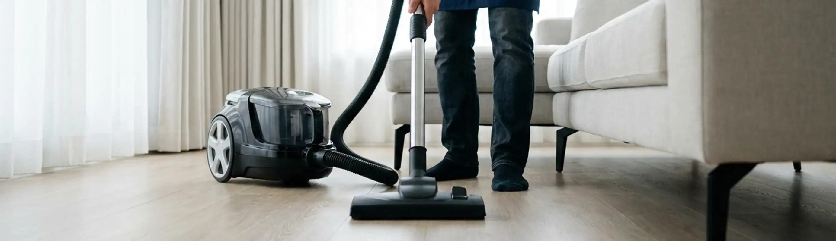Professional house cleaner vacuuming a living room floor with a canister vacuum cleaner, Dayton, OH.