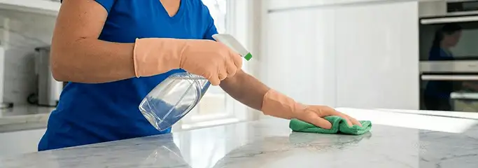 Maid service worker spraying and wiping a kitchen countertop with a microfiber cloth for sanitizing, Dayton, OH.