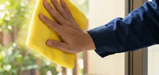 House cleaner wiping a glass window with a yellow microfiber cloth for streak-free cleaning, Dayton, OH.